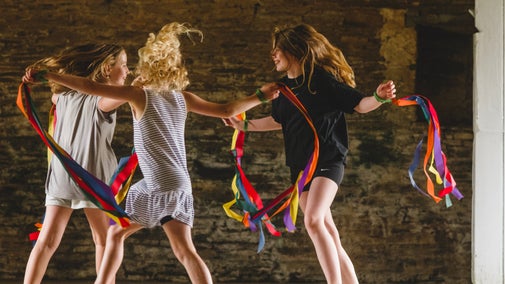 Three young teenage children are dancing in a circle with colourful ribbons.